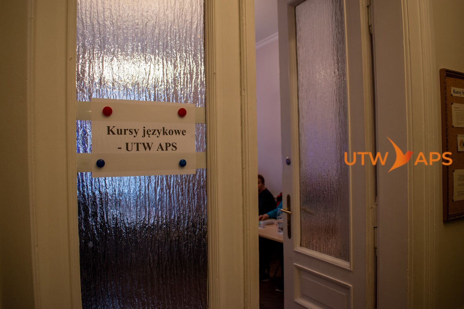Drzwi na pierwszym piętrze z kartką Kursy językowe UTW APS